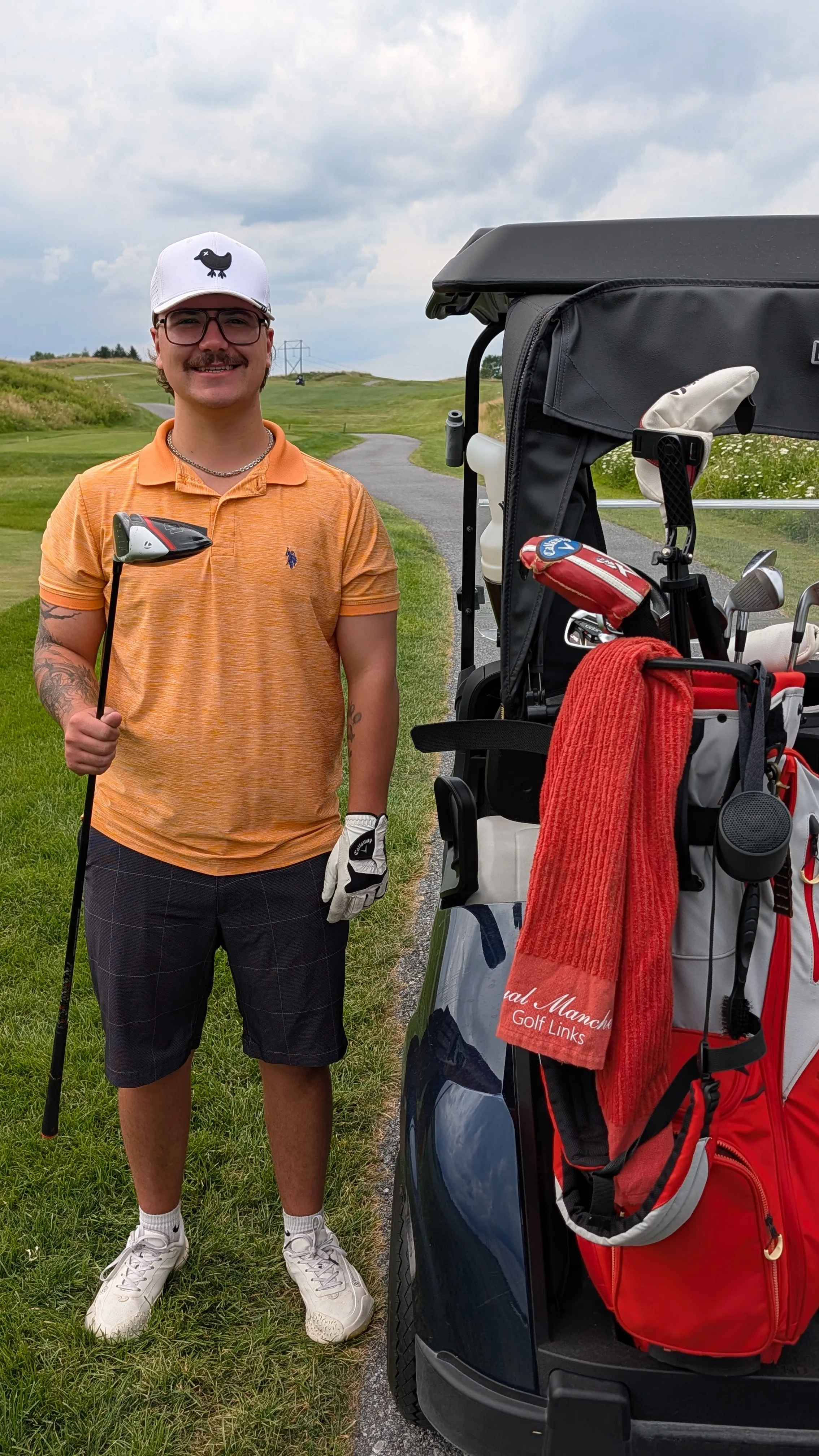 Ty of Flash Avenue smiling on the golf course, driver in hand, next to a cart loaded with his clubs